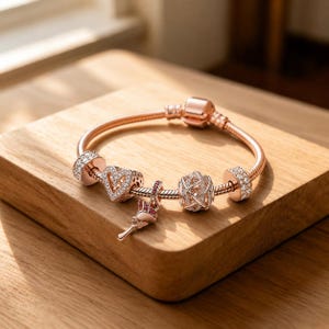 May include: A rose gold charm bracelet featuring a series of decorative beads, including a heart-shaped charm with clear stones, a dangling rose-shaped charm with pink accents, a spherical openwork charm, and two cylindrical spacers with clear stones.