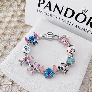 Può includere: Un bracciale con ciondoli in argento caratterizzato da molteplici ciondoli in smalto colorato che raffigurano il personaggio Stitch in varie pose, insieme a un ciondolo a forma di cuore con il testo 'Love You', su una catena a serpente.