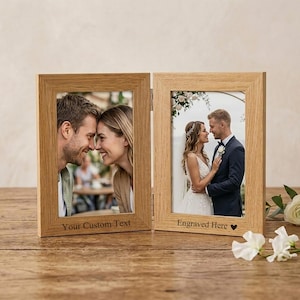 May include: A hinged double photo frame made of light-colored wood with a visible grain. The left frame features the text "Your Custom Text" and the right frame features the text "Engraved Here" followed by a small heart symbol.