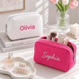 Può includere: Una borsa cosmetica bianca con trama a cialda e il nome Olivia ricamato in rosa, e una borsa cosmetica rosa acceso con trama a cialda e il nome Sophia ricamato in bianco, entrambe dotate di cerniere metalliche color argento.