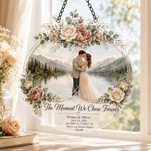 May include: A circular acrylic hanging ornament featuring a printed landscape of a couple embracing by a lake and mountains. The design is framed by watercolor roses and greenery. Text reads: The Moment We Chose Forever, Emma & Oliver, June 14, 2026, 40.7484 N, 73.9857 W.