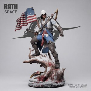 Puede incluir: Una figura detallada de un personaje con capucha en un traje azul y blanco, sosteniendo una bandera estadounidense histórica con trece estrellas. La figura se apoya sobre una base de tronco de árbol nevado. Texto RATH SPACE y CRAFTED IN SPACE PRINT ON EARTH.