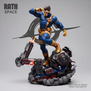 Op de afbeelding: Een verzamelfiguur van een superheld in een blauw en geel pak met een vizier, staand op een mechanische basis met rookeffecten. De tekst RATH SPACE staat linksboven en CRAFTED IN SPACE PRINT ON EARTH staat rechtsonder.
