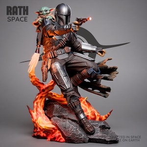 Könnte beinhalten: Eine detaillierte Figur eines gepanzerten Kriegers mit silbernem Helm und braunem Anzug, der eine kleine grüne Kreatur auf dem Rücken trägt. Die Figur hält einen Blaster mit rotem Lichteffekt auf einem felsigen Sockel mit orangefarbenen Flammen.