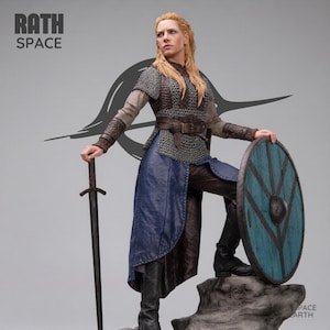 May include: A detailed collectible figurine of a warrior with long blonde hair, wearing chainmail, a brown leather belt, and a blue tunic. The figure holds a long sword in one hand and rests a foot on a round blue and black shield. Text reads RATH SPACE.