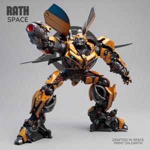 Può includere: Un action figure robotica gialla e nera con dettagli meccanici, occhi blu e un'arma sul braccio destro. Il testo RATH SPACE appare nell'angolo in alto a sinistra e CRAFTED IN SPACE PRINT ON EARTH è scritto nell'angolo in basso a destra.