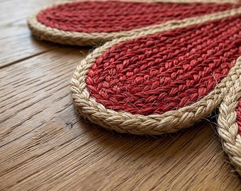 May include: A flower-shaped placemat crafted from woven red fiber with a thick, braided natural tan jute border. The petals are arranged in a circular pattern, showcasing a textured, fibrous surface with a distinct contrast between the red center and the tan edge.
