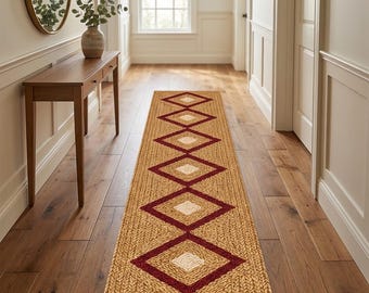 May include: A long, rectangular runner rug featuring a woven tan texture with a repeating pattern of dark red diamond shapes, each containing a smaller, lighter cream-colored diamond center, laid flat on a wooden floor in a hallway.