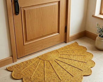 May include: A semi-circular mustard yellow rug with a textured, braided knit pattern radiating from the center in a sunburst design. The edges of the rug feature a scalloped border, creating a rounded, decorative shape on the floor.