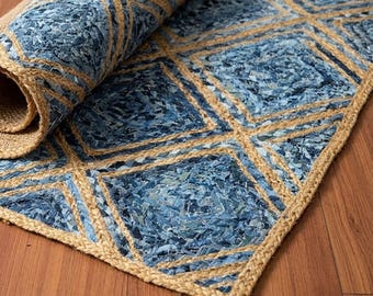 May include: A rectangular area rug featuring a geometric diamond pattern created with natural tan jute fibers and textured blue fabric scraps. The rug is partially rolled at one end, revealing the woven jute backing and the layered blue material.