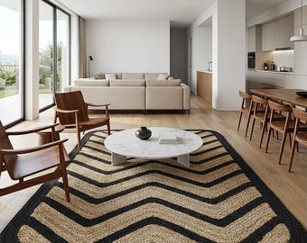 May include: A rectangular area rug featuring a repeating chevron pattern in natural tan and black fibers. The rug has rounded corners and a thick black border, positioned on a light wood floor in a living room setting.