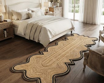 May include: A long, rectangular jute runner rug featuring a natural tan woven texture and a distinct scalloped edge outlined with a thick black border. The rug is positioned on a dark wood floor in front of a bed with white bedding.