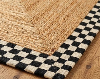 May include: A rectangular area rug featuring a central section of woven tan jute fibers. The rug is bordered by a distinct black and white checkered pattern that frames the natural textured material, creating a clear contrast in design.