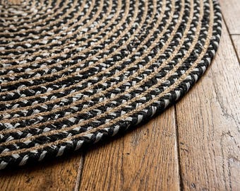 May include: A circular braided rug featuring a repeating pattern of thick, twisted strands in black, white, and natural tan fibers. The rug is constructed from concentric coils that create a textured, dense surface with a consistent woven appearance.
