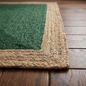 Puede incluir: Una alfombra rectangular con una sección central de color verde bosque profundo hecha de fibras naturales tejidas, rodeada por un borde ancho y grueso de yute trenzado de color tostado. La alfombra tiene una textura orgánica y un contraste.
