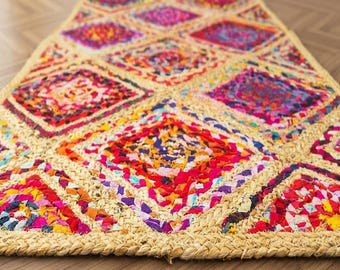 May include: A rectangular area rug featuring a braided natural fiber border and a central pattern of diamond shapes filled with multicolored fabric scraps in shades of pink, red, blue, yellow, and purple, creating a textured surface.