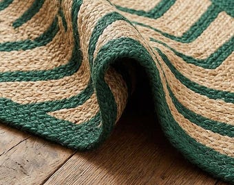 May include: A woven rug featuring a textured, natural tan fiber base with a bold, dark green chevron pattern. The rug is folded over, revealing the thick, braided construction of the material and the consistent geometric design.