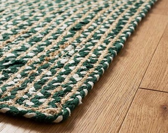 May include: A rectangular area rug featuring a braided construction with alternating strands of dark forest green, natural tan, and crisp white fibers. The woven texture creates a dense, repeating pattern across the entire surface of the floor covering.