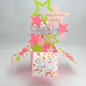 May include: A pink pop-up card with a "Sweet 16" theme. The card features pink, green, and silver star cutouts, with the words "Happy Birthday Olenka!" and "Sweet" displayed. The card is decorated with colorful confetti.