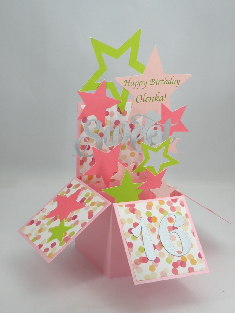 May include: A pink pop-up birthday card with star cutouts in pink and green. The card features the word "Sweet" and the number "16" in silver, along with the text "Happy Birthday Olenka!" on a star.