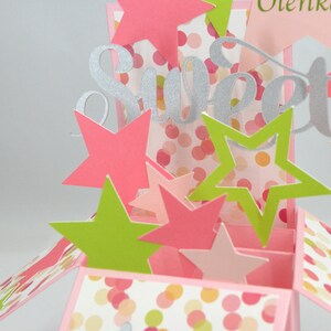 May include: A pop-up card with a pink and white polka dot pattern, featuring the word "Sweet" in silver glitter. The card is decorated with pink and green star cutouts, creating a festive and celebratory design.