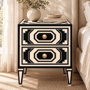 May include: A two-drawer nightstand featuring a bold black and cream geometric pattern. The piece has a rectangular frame, tapered legs, and two faceted gold-toned knobs. The top surface displays a matching octagonal inlay design.