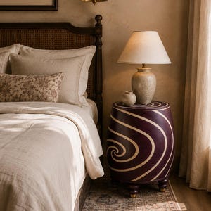 May include: A barrel-shaped side table featuring a deep purple finish with a prominent cream-colored spiral pattern. The table is supported by four small, rounded feet and serves as a base for a ceramic lamp and a small, matching decorative bowl.