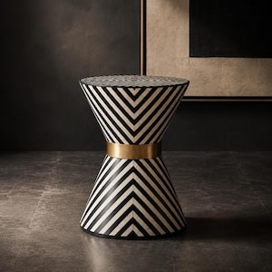May include: An hourglass-shaped side table featuring a black and white chevron pattern across its surface. The table has a circular top and a tapered base, connected in the centre by a smooth, wide, metallic gold band that encircles the middle.