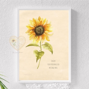 May include: A framed wall art print featuring a watercolour illustration of a single yellow sunflower with a dark brown centre and green leaves on a light beige background. The text "Insert your personalised message here" is printed in black.