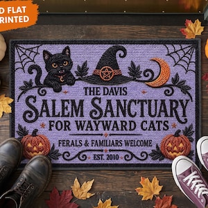 Peut inclure: Un paillasson rectangulaire à fond violet texturé en tricot avec un chat noir, un chapeau de sorcière, un croissant de lune et deux citrouilles. Le texte indique : THE DAVIS SALEM SANCTUARY FOR WAYWARD CATS, FERALS & FAMILIARS WELCOME, EST. 2010.