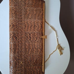Könnte beinhalten: Eine rechteckige Clutch mit braunem Schlangenledermuster und einem vertikalen, strukturierten Einsatz. Die Tasche verfügt über einen goldfarbenen Metallrahmen, einen zentralen dreieckigen Verschluss und eine feine Goldkette als Trageriemen.