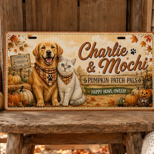 May include: A rectangular metal sign featuring a golden retriever and a grey cat wearing plaid bandanas. The text reads Charlie & Mochi, PUMPKIN PATCH PALS, and HAPPY HOWL-OWEEN! The background shows a pumpkin patch with autumn leaves and pumpkins.