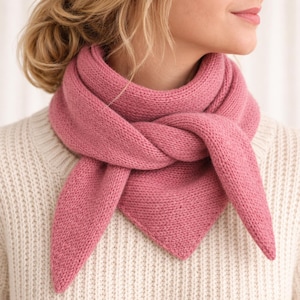 May include: A solid dusty rose pink triangular knit scarf with a textured garter stitch pattern. The scarf is wrapped around the neck and tied in a knot at the front, with two pointed ends hanging down over a cream-colored ribbed knit sweater.