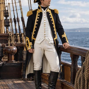 Op de afbeelding: Een marineofficiersuniform bestaande uit een zwarte lange jas met gouden biezen, gouden knopen en gouden epauletten, gedragen over een wit vest en een witte broek. De outfit bevat een zwarte steekhoed met gouden biezen en hoge zwarte leren laarzen.