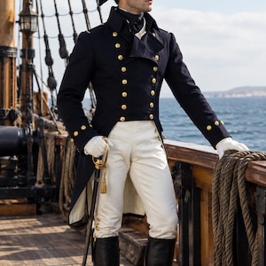 Puede incluir: Una casaca militar azul marino con botones dorados, pantalones blancos y un sombrero bicornio negro con adornos dorados. El conjunto incluye guantes blancos, botas altas de cuero negro y una espada con empuñadura dorada al costado.
