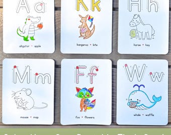 Könnte beinhalten: Sechs weiße Lernkarten mit Groß- und Kleinbuchstaben sowie nummerierten Strichführungen. Jede Karte zeigt eine farbige Illustration eines Tieres und eines Objekts, die dem Buchstaben entsprechen, mit Beschriftungen wie Alligator, Apfel, Känguru, Drachen, Pferd, Heu, Maus, Karte, Fuchs, Blumen, Wal und Waffel.