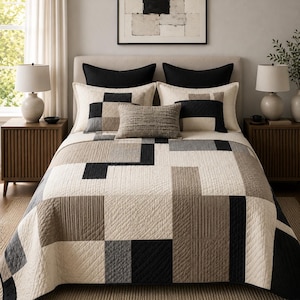 May include: A quilted bedspread featuring a geometric pattern of cream, beige, gray, and black rectangular blocks. The bedding set includes two large black pillows, two cream-colored shams, and a small rectangular textured accent pillow.