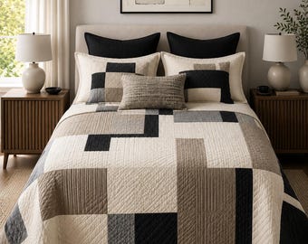 May include: A quilted bedspread featuring a geometric pattern of cream, beige, gray, and black rectangular blocks. The bedding set includes two large black pillows, two cream-colored shams, and a small rectangular textured accent pillow.