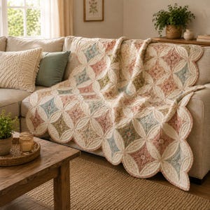 May include: A quilted throw blanket featuring a repeating pattern of cream-colored circles and diamond-shaped inserts in muted shades of dusty rose, sage green, and slate blue. The blanket has a scalloped edge and intricate stitching throughout.
