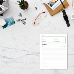 May include: A white paper document titled Official Homeschool Transcript with fields for student information and a course record section with horizontal lines, positioned on a white marble surface with various office supplies scattered around.