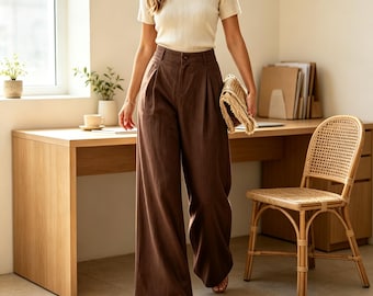 Puede incluir: Un top de manga corta acanalado de color crema con escote cuadrado combinado con pantalones de pierna ancha de color marrón oscuro de talle alto con pliegues delanteros y cierre de botón. El conjunto se completa con sandalias planas y un bolso de mano beige.