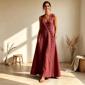 Puede incluir: Un vestido largo sin mangas de color rojo terracota intenso. El vestido presenta un escote en V, un corpi&ntilde;o ajustado y una tapeta de botones diagonal que va desde el hombro hasta la cintura, con una falda amplia y fluida y bolsillos laterales.