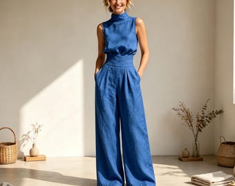Puede incluir: Un mono azul sin mangas con cuello alto, cintura entallada con una banda ancha y pantalones de pierna ancha. La prenda está confeccionada en tela azul lisa e incluye bolsillos laterales, lo que proporciona una silueta limpia y estructurada.