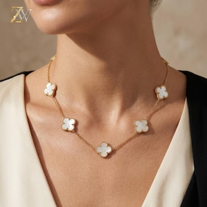 May include: A gold chain necklace featuring five evenly spaced, four-leaf clover-shaped charms. Each charm is inlaid with a smooth, white iridescent material and bordered by a thin gold beaded edge, connected by a delicate gold link chain.