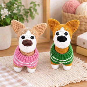 Op de afbeelding: Twee handgemaakte gehaakte hondjes met puntige oren en zwarte plastic ogen. De ene hond draagt een roze trui met witte horizontale strepen, de andere een groene trui met witte horizontale strepen. Beide hebben witte snuiten.
