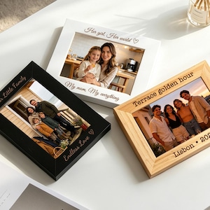 Puede incluir: Tres marcos de fotos rectangulares con acabados en negro, blanco y madera natural. Cada marco presenta texto grabado con láser. El marco negro dice Our Little Family y Endless Love. El marco blanco dice Her girl, Her world y My mom, My everything. El marco de madera dice Terrace golden hour y Lisbon 2026.
