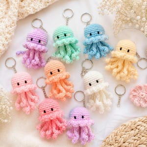 Peut inclure: Un ensemble de neuf porte-clés méduse crochetés dans diverses couleurs pastel, notamment lavande, vert menthe, bleu clair, jaune pâle, rose tendre, pêche et blanc. Chaque méduse présente une tête ronde, des yeux noirs et des tentacules bouclés.