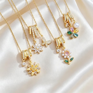 May include: Four gold-tone necklaces featuring pendants with clear cubic zirconia stones. The pendants include floral and butterfly motifs, with one featuring a white pearl and multi-colored stones. Each necklace has a delicate gold-tone chain.