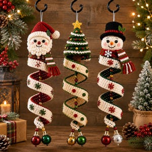 May include: Three hanging crochet Christmas ornaments featuring a Santa Claus, a decorated Christmas tree, and a snowman. Each figure is attached to a long, spiraling cream-colored ribbon adorned with small red and green snowflake patterns.
