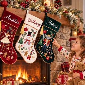 May include: Three personalised Christmas stockings hanging in a row. The left is deep red with the name Amelia, the centre is cream with the name Bethany, and the right is dark green with the name Robert. Each features gold tassels and embroidery.